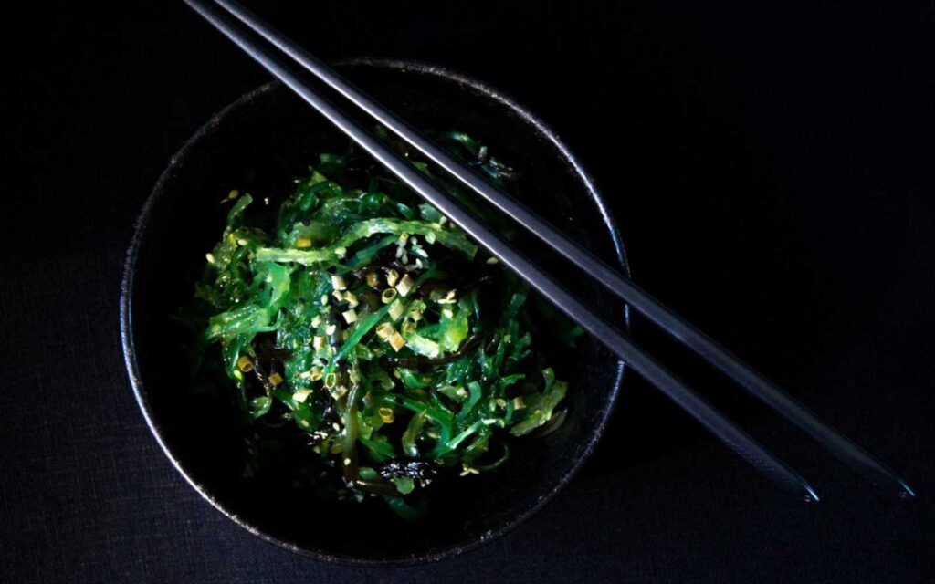 alghe giapponesi wakame in ciotola nera con bacchette nere