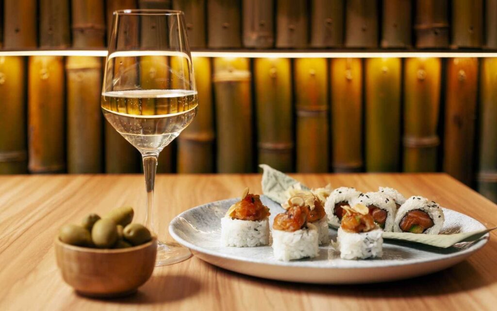 calice di vino bianco con ciotola di edamame e piatto con sushi roll vari
