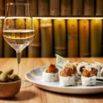 calice di vino bianco con ciotola di edamame e piatto con sushi roll vari